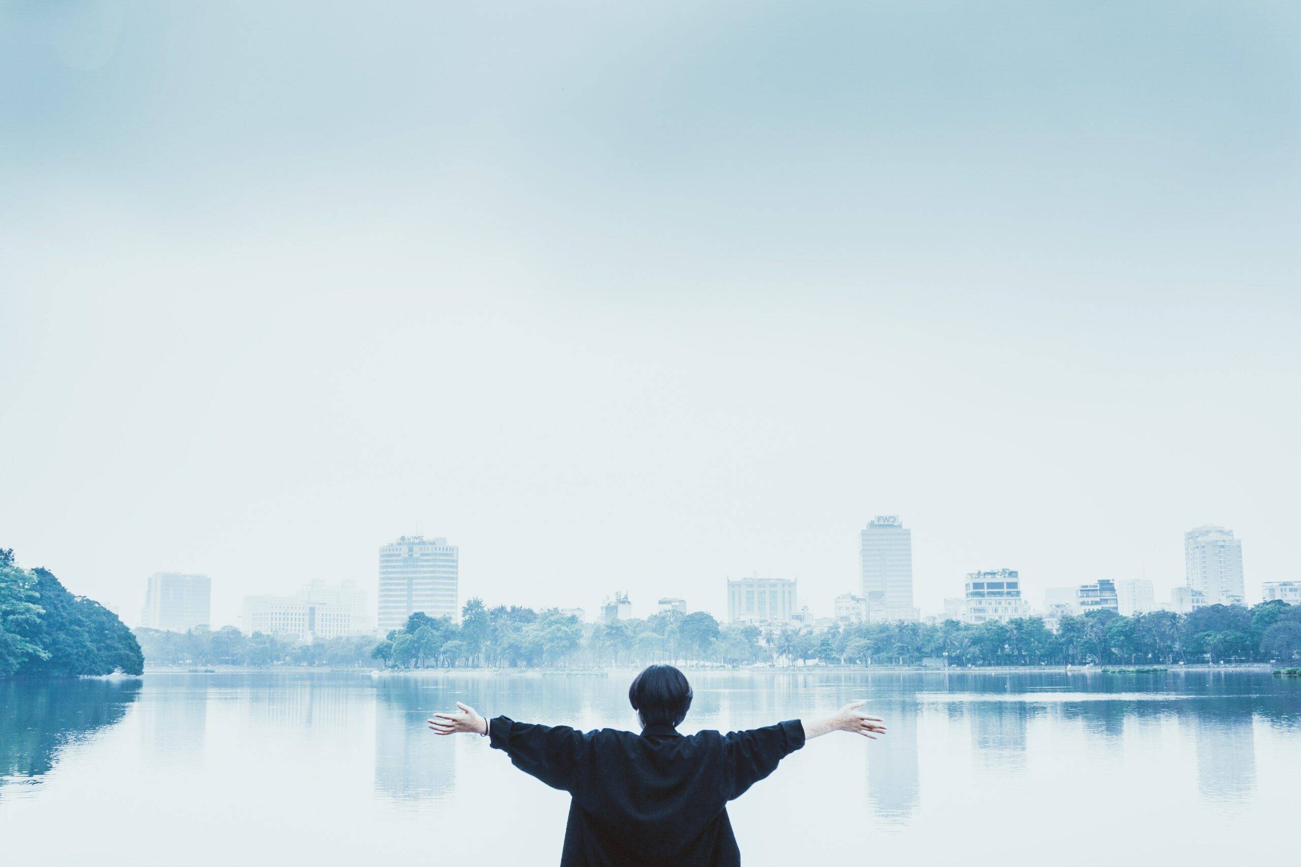 person facing a lake and city scape with arms wide open