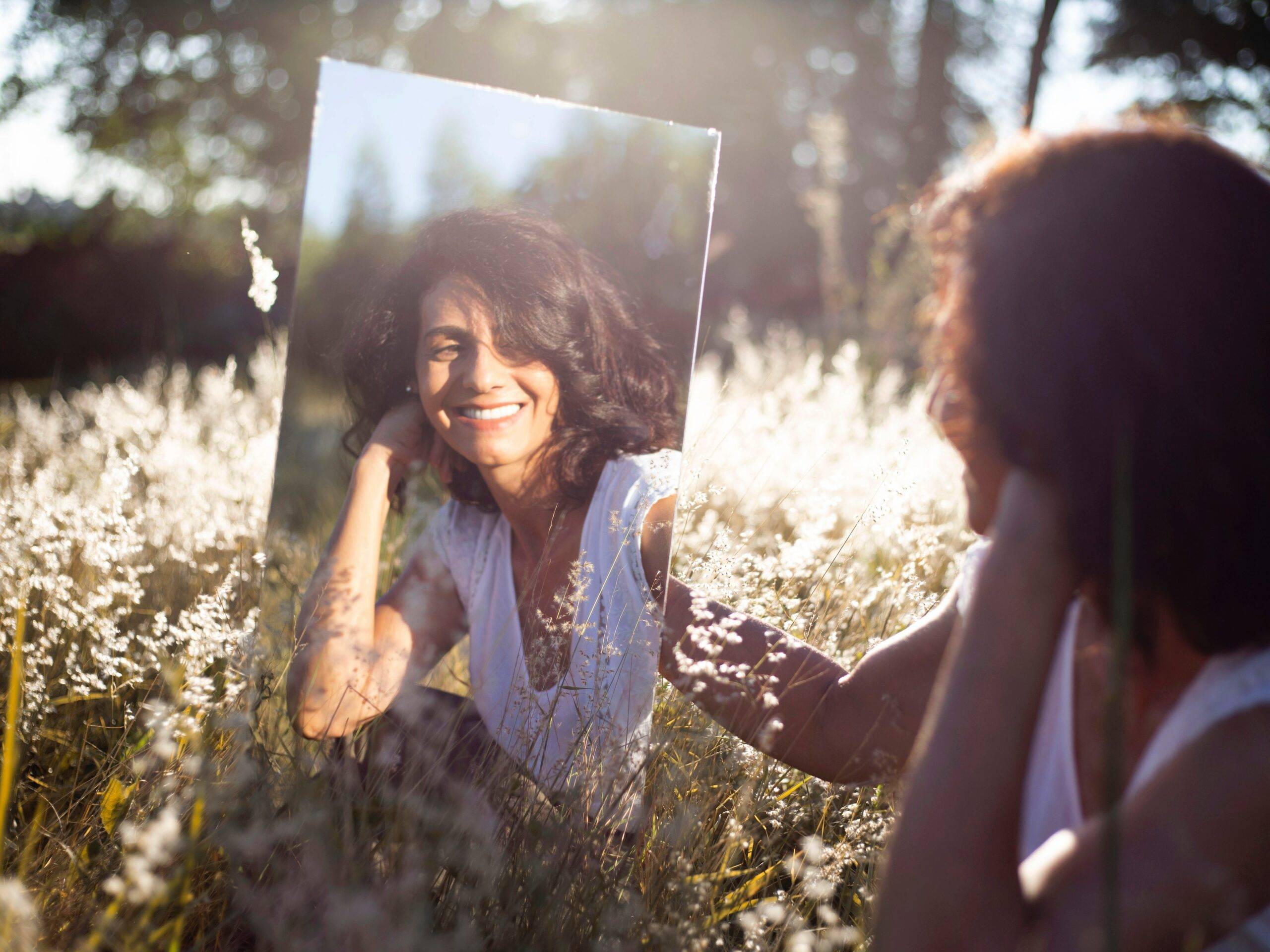 Woman looking at her reflection in a mirror in the middle of an open field