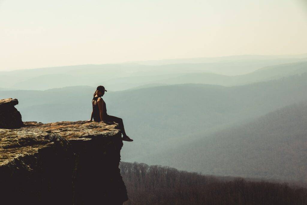 Woman sitting at top of mountain cliff with feet hanging over the edge
